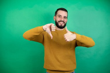 Yeşil arka planda rahat kıyafetler giyen yakışıklı bir adam. Baş parmak hareketi yapıyor. Anlaşmazlık ve uzlaşma ifadesi. Çılgın çatışma