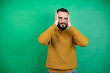 Yeşil arka planda rahat kıyafetler giyen yakışıklı bir adam yorgun ve sıkılmış görünüyor.