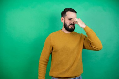 Yeşil arka planda rahat kıyafetler giyen yakışıklı bir adam pis ve iğrenç bir koku alıyor. Dayanılmaz bir koku. Parmakları burnunda nefesini tutuyor.