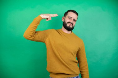 Yeşil arka planda rahat kıyafetler giyen yakışıklı bir adam. Kendini vuruyor ve öldürüyor. Silah gibi el ve parmaklarını işaret ediyor..