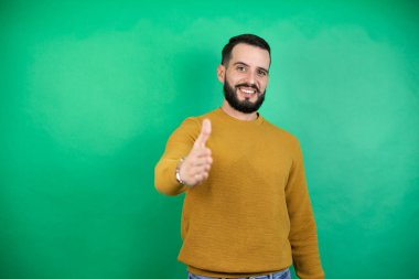 Yeşil arka planda rahat kıyafetler giyen yakışıklı adam dostça bir selamlama ve hoş geldin hediyesi olarak gülümsüyor.