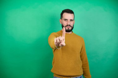 Yeşil arka planda rahat kıyafetler giyen yakışıklı bir adamın bir numaralı parmaklarıyla işaret etmesi ciddidir.