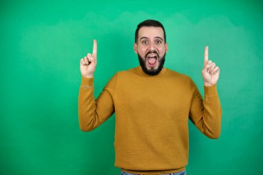 Yeşil arka plan üzerinde günlük giysiler giyen yakışıklı bir adam kameraya bakıp parmaklarını kaldırıp kollarını kaldırdığında şaşırmış ve şaşırmıştı.