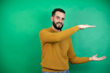 Yeşil arka plan üzerinde sıradan kıyafetler giyen yakışıklı bir adam. Ellerinde büyük ve büyük bir işaret, ölçü işareti var. Gülümsüyor. Ölçüm konsepti.