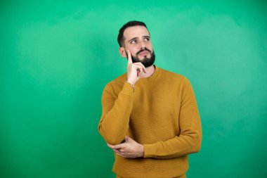 Yeşil arka plan üzerinde sıradan kıyafetler giyen yakışıklı bir adam ciddi bir yüz ifadesi olan eli çenesinde soru soran, kafa karıştırıcı bir fikir hakkında düşünceli biri.