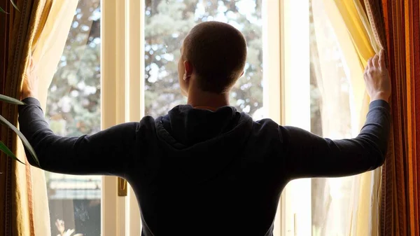Rear View of a Man with Standing and Drawing the Curtains at Home, Quarantine Lockdown