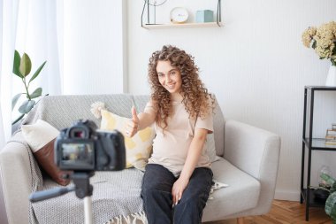 Bekleyen mutlu anne rahat bir atmosferde koltukta oturup abonelerine kamera ve tripodla video kaydediyor. Hamilelik, teknoloji ve blog konsepti.