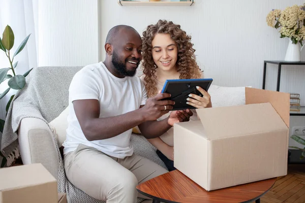 stock image Having settled down comfortably at home on the sofa, the future mommy and her husband joyfully consider the printed photo brought by the courier in the box. Pregnancy, family and joy concept.