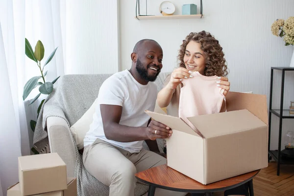 Future parents received a parcel of an order from the online store, unpacking a box of clothes for the unborn daughter. Pregnancy, family, online shopping concept.