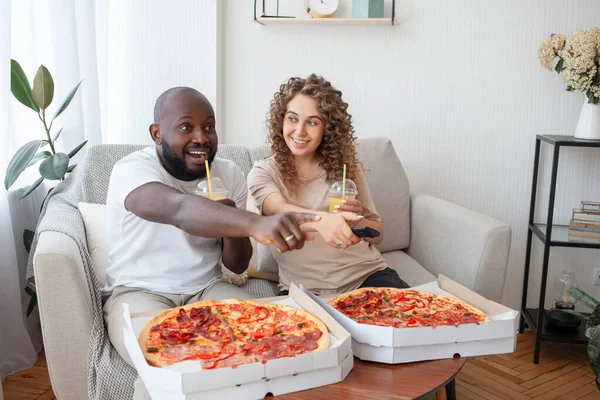 Entertain a wonderful modern couple in the living room while watching an exciting program on TV. For dinner delicious pizza and a glass of orange juice. Rest, family, food and pregnancy concept.