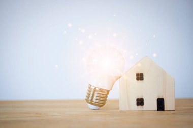 Masada model ahşap evi olan ampul, tasarruf, yeni ev, yeni fikir, yeni teknoloji yüksek yenilik, mülk ve ipotek mavi gökyüzü arka planında.