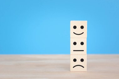 Tahta bloklar yüz ikonu duygusunu, mutluluğu, üzüntüyü, üzüntüyü, mavi arka planda izole edilmiş farklı düşünceleri gösteriyor..