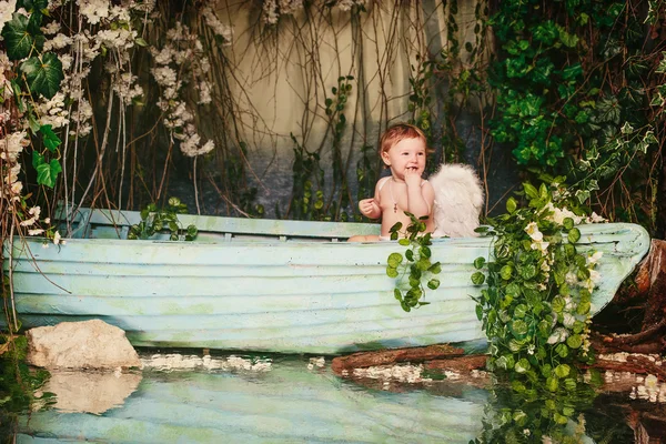 Baby with angel wings in a boat with flowers — Stock Photo, Image