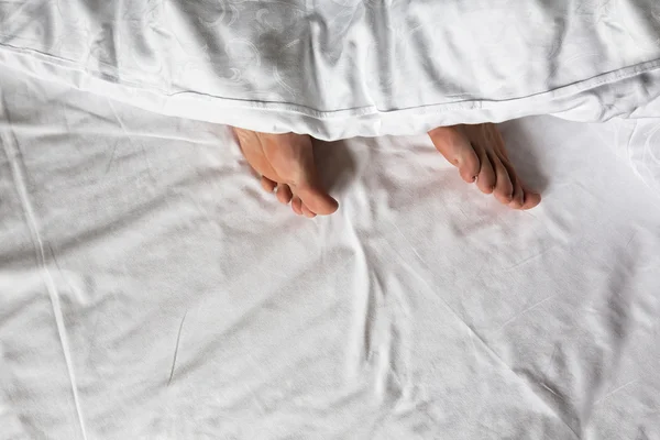 Piernas en la cama debajo de la manta —  Fotos de Stock