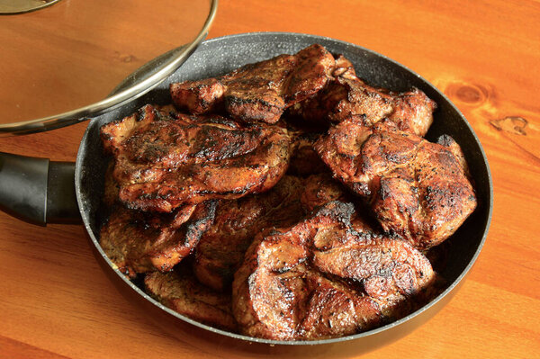 Juicy pork steaks in black skillet resting on rustic wooden kitchen table. High quality photo