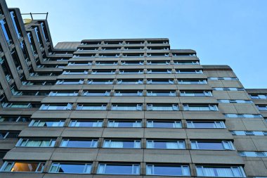 Simetrik pencereleri ve mavi gökyüzü olan acımasız beton bina perspektifi.