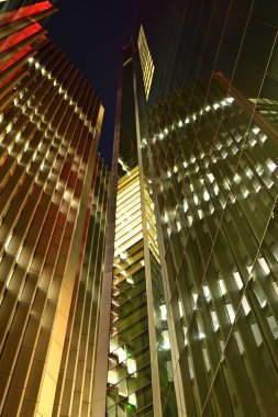 Şehir manzarası yansıtıcı cam cepheleriyle aydınlatılmış modern gökdelenleri gösteriyor..