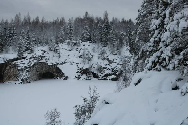 冬の岩を背景にした雪に覆われた斜面で 森林湖の近くに洞窟があります — ストック写真