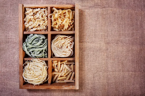Assorted pasta in wooden box catalog on dark fabric background