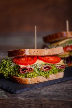 Marul ile tahıl ekmek ile iki sandviç, taze domates ve tatlı biber, salam, jambon, salam, peynir ve soğan dilimleri karanlık mermer arka plan üzerinde filizlenir. Yakın çekim