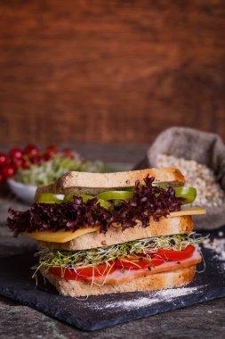 Marul ile tahıl ekmek, dilim taze domates ve karanlık mermer zemin üzerine tatlı biber, salam, jambon, salam, peynir ve soğan lahanası ile sandviç. Yakın çekim