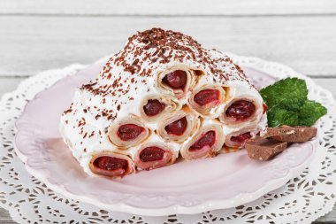 Krema, vişne ve hafif ahşap arka plan üzerinde tabakta rendelenmiş çikolata ile haddelenmiş krep pasta. Seçici odak