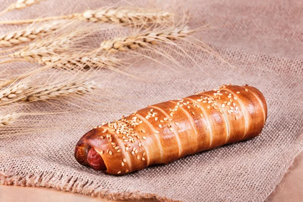 Хот-дог с кунжутом семян на деревенском фоне с шипами. Выпечка и хлеб в пекарне — стоковое фото