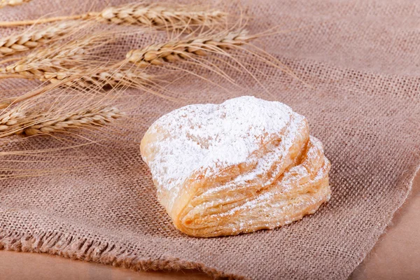 Friss leveles tészta porcukorral a rusztikus háttér spikelets. Süteményeket és kenyeret egy pékség — Stock Fotó