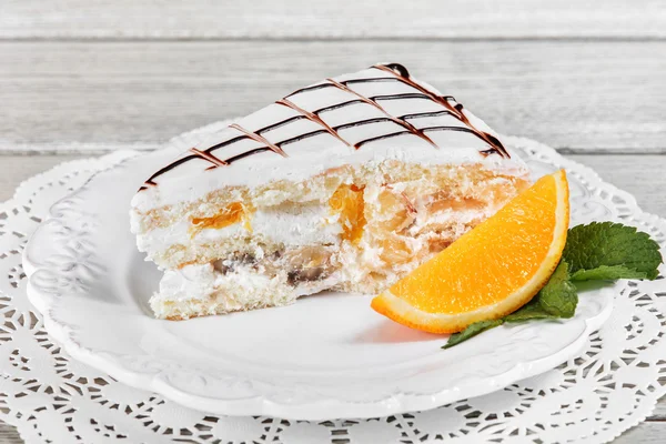 Торт со взбитыми сливками, с бананом и апельсином на тарелке, на светлом деревянном фоне. Селективный фокус — стоковое фото