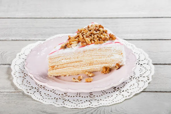 Медовый торт с грецкими орехами на тарелке, на светлом деревянном фоне. Селективный фокус — стоковое фото