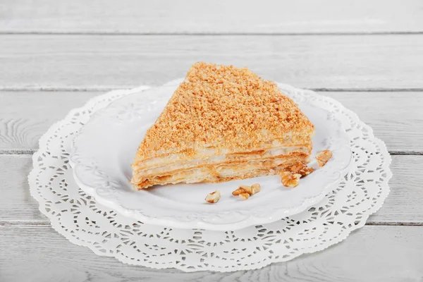 Cake Napoleon with sour cream and walnuts on plate, on a light wooden background. Selective focus — Stock Photo, Image