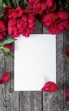 Beyaz kağıt kart, pembe şakayıklar ve ahşap arka planda taç yaprakları. Selamlama için boş alan