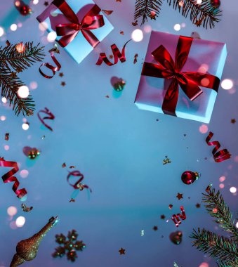 Mutlu Noeller ve yeni yıl geçmişi. Uçan süslemelerden yapılmış Noel kartı, köknar dalları, toplar, kar taneleri, ışıltılar, hediye kutuları, renkli neon mavi ve mor arka planda bokeh