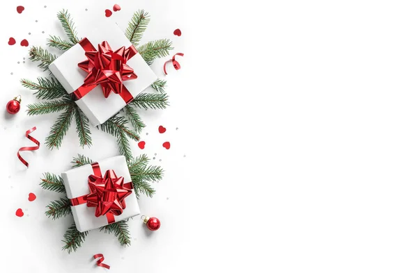 Noel ağacı dalları, kırmızı kurdeleli hediye kutuları, kırmızı süslemeler, parıltılar ve beyaz arka planda konfeti. Noel ve yeni yıl tebrik kartı, kış tatili. Düz konum, üst görünüm, çerçeve