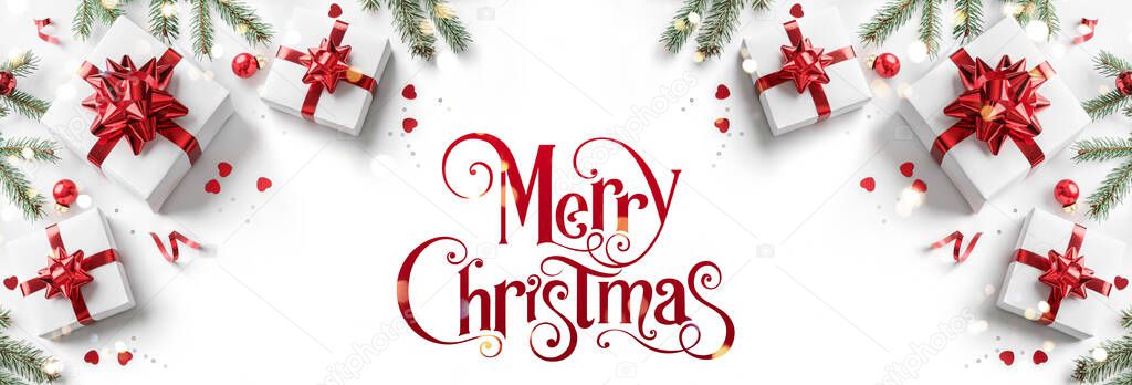 Merry Christmas text on white background with gift boxes, ribbons, red decoration, fir branches, bokeh, sparkles and confetti. Xmas and New Year greeting card, bokeh, light. Flat lay, top view, banner