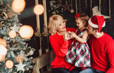 Mutlu Noeller ve mutlu yıllar! Aile, oturma odasında Noel ağacı ve Noel hediyesi kutularıyla süslenmiş bebeğe hediye kutusu veriyor. Portre seven aile yakın çekim, tatil