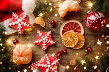 Noel kurabiyesi yıldızları, köknar dalları, kırmızı süslemeler, ışık çelenkleri, Noel Baba şapkası, turuncu ve tahta arka planda hediye kutuları. Mutlu Noeller ve yeni yıl tatili. Xmas kurabiyeleri, üst manzara, bokeh
