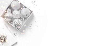 Hediye kutusundan, beyaz ve gümüş süslemelerden, köknar dallarından, parıltılardan ve beyaz arka planda konfetiden oluşan mutlu Noeller kartı. Noel ve Yeni Yıl tatili, Bokeh, ışık. Düz yatış, üst görünüm