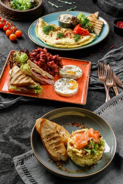 Yumurtalı, sebzeli, salata yapraklı, sosisli ve tostu koyu arkaplanda servis edilen lezzetli kahvaltı yemekleri. Kapatın. Sağlıklı kahvaltı kavramı