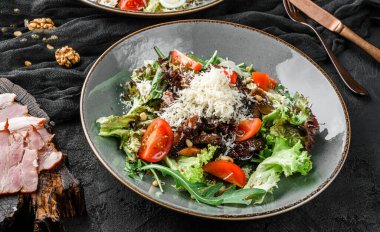 Domatesli, yeşil yapraklı ve koyu arkaplanda parmesanlı balzamik soslu lezzetli biftek salatası. Sağlıklı vejetaryen yemekleri, temiz yemek, perhiz, üst manzara.