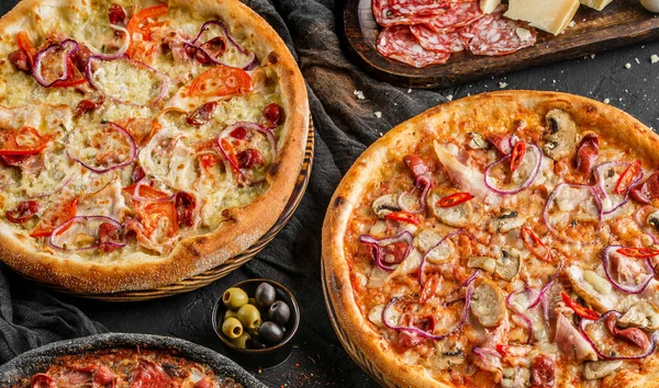 Variety of meat pizzas with sausage, ham, prosciutto, salami, chicken fillet, pepperoni, cheese, greens, vegetables on wooden board on black background. Fast food lunch for picnic company, top view