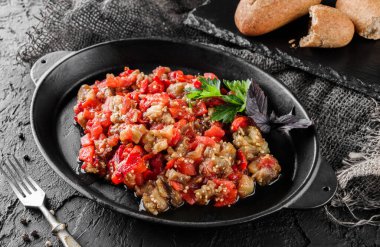 Biberli ve domatesli lezzetli patlıcan salatası. Büyük tabakta, koyu arkaplanda. Sağlıklı vejetaryen yemekleri, temiz yemek, üst manzara.