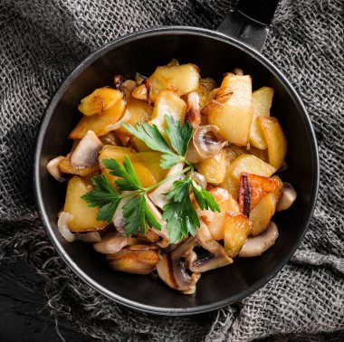 Ev yapımı, mantarlı patates kızartma tavasında maydanozlu, koyu arka planda, üst tarafta.