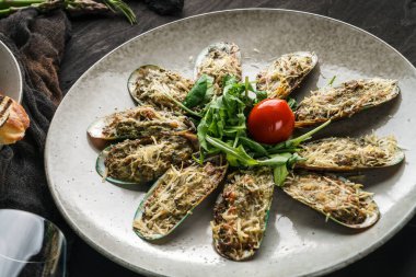Koyu arkaplanda servis edilen ıspanaklı ve parmesanlı fırında midye. Deniz ürünleri konsepti, sağlıklı yiyecekler, üst manzara.