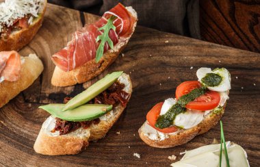 Prosciutto, somon, domates, mozzarella, parmesan peyniri, avokado ve fesleğen ve bir bardak şarapla birlikte taze bruschetta. Atıştırmalık sandviçler, kapatın.