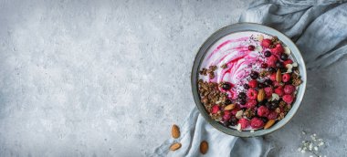 Yoğurt, granola, müsli, tohum, donmuş ahududu, yabanmersini ve açık arkaplanlı mavi seramik fındıklı sağlıklı kahvaltı kasesi. Sağlıklı yiyecekler, detoks pürüzsüz, vejetaryen beslenme, üst görüş.
