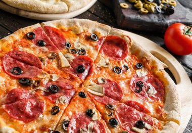 Prosciutto, sosis, jambon, peynirli parmesan peyniri, domates, mantar, koyu ahşap arka planda zeytinli pizza. Piknik şirketi için fast food, yakın çekim, seçici odaklanma