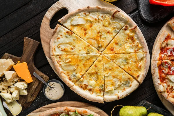 Four cheese pizza quattro formaggi with parmesan, brie, gouda, mozzarella cheese and pear on wooden board on black background. Vegetarian pizza, top view
