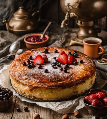 Ev yapımı cheesecake veya böğürtlenli süzme peynir güveci ve kırsal ahşap masa üzerinde semaver ve çaydanlık ile krema şekeri, kompleks kompozisyon. Tatlı tatlı, kapat.