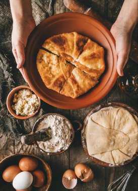 Düz ekmek tutan eller ya da süzme peynirli yuvarlak turtalar, yumurtalar, kırsal ahşap arka planda tabakta bitki. Ev yapımı pişirme, sağlıklı gıda konsepti, üst görünüm, tonlama